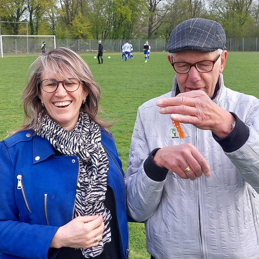 Twee supporters bij een sportveld, met Keyco-pin zichtbaar
