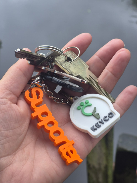 Hand met sleutelbos, Keyco-logo en oranje Supporter-hanger
